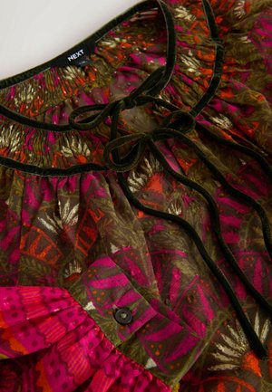 Multifarvet bluse med blomsterprint i pink, grøn og orange, med en samlet halsudskærm og sorte fløjl-bånd detaljer. Knapdetailer synlige.