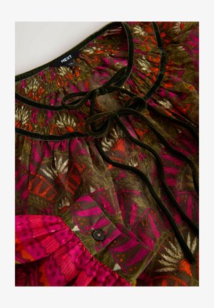 Blusa multicolore con motivo floreale in rosa, verde e arancione, con scollatura arricciata e dettagli in velluto nero a fiocco. Dettaglio dei bottoni visibile.
