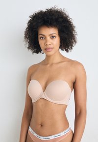 Nude strapless bra with smooth fabric, molded cups, and a seamless design. Features Calvin Klein logo on waistband of matching underwear.