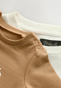 Brązowe i białe prążkowane swetry z okrągłym dekoltem, z zatrzaskami na ramionach, jeden oznaczony jako odzież ciążowa.