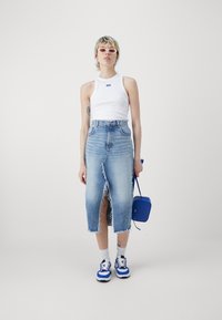 Högmidjad ljusblå denimkjol med fransad fåll och framtillslits, i kombination med en vit ärmlös topp och blå accessoarer.