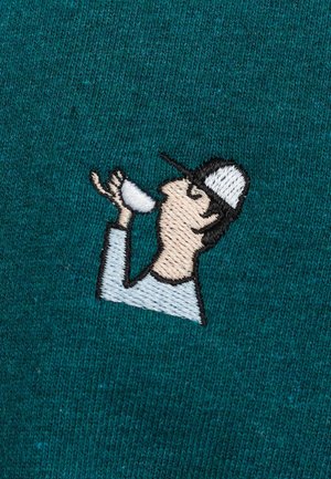 Knitted teal fabric features an embroidered design of a person with a cap, holding a cup, in neutral tones with outlined details.