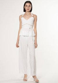 Witte jumpsuit met een aansluitend lijfje, halterbanden en een peplum taille. Wijde broekspijpen en subtiele decoratieve accenten maken het ontwerp compleet.