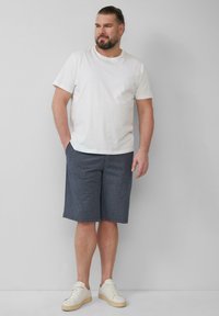T-shirt en coton blanc, shorts à carreaux bleu marine et baskets blanches. Les shorts sont de longueur genou avec des poches latérales. Design simple et décontracté.