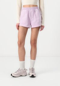 Lys lilla bomulds shorts med elastisk talje, to sidelommer og en løs pasform, parret med lyse grå sneakers og hvide sokker.