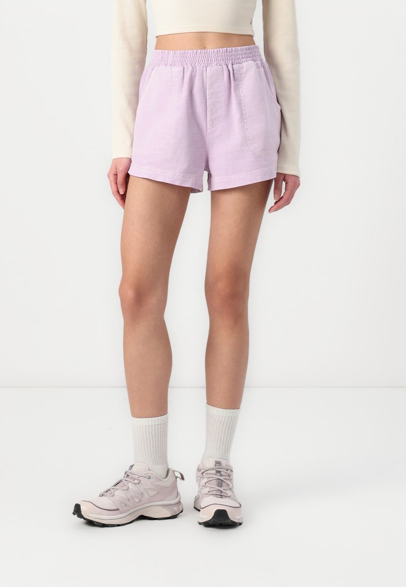 Lys lilla bomulds shorts med elastisk talje, to sidelommer og en løs pasform, parret med lyse grå sneakers og hvide sokker.