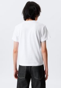 White cotton t-shirt with short sleeves and a relaxed fit, paired with dark denim jeans featuring contrasting stitching and back pockets.