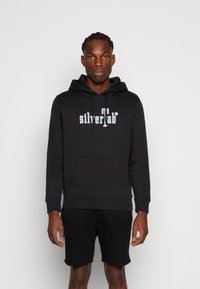 Zwarte capuchontrui met een voorzak en elastische boorden, met het "silverTab" logo in lichtblauw en wit. Zachte stofstructuur.