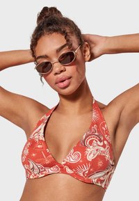 Top de bikini triangular rojo con un patrón paisley, diseño de cuello halter y una textura suave. La modelo lleva gafas de sol ovaladas pequeñas.