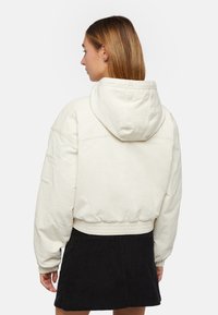 Cremefarvet cropped hoodie med snøre i huen, elastisk kant og ribbede manchetter. Har en sidelomme og blødt tekstureret stof.