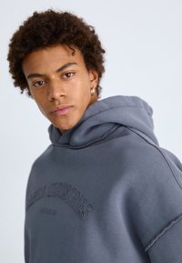 Sweat-shirt à capuche gris avec un détail de logo brodé, texture douce et coupe décontractée avec une grande capuche.