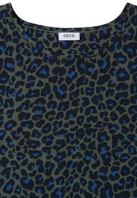 Gros plan sur un tissu vert avec un imprimé léopard noir et bleu et une étiquette blanche de marque CECIL au niveau de l'encolure ronde.