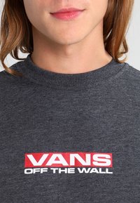 Tummanharmaa collegepaita resorikauluksella. Edessä punainen "VANS OFF THE WALL" -logo. Pehmeä kangastuntuma.