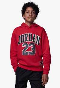 Rød hettegenser laget av bomull med en frontgrafikk "JORDAN 23" i fet svart og hvit skrift. Har en kengurulomme og justerbar hette.