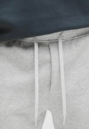 Nahaufnahme von grauen Jogginghosen mit weißen Kordeln, getragen mit einem dunkel gefärbten Oberteil.