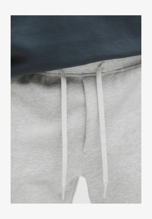 Primo piano di pantaloni della tuta grigi con lacci bianchi annodati, indossati con una maglia di colore scuro.