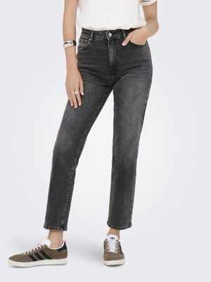 Schwarze hochgeschnittene Jeans mit geradem Bein, ausgestattet mit Knopfverschluss, fünf Taschen und einer leicht verwaschenen Optik. Getragen mit braunen und weißen Turnschuhen.