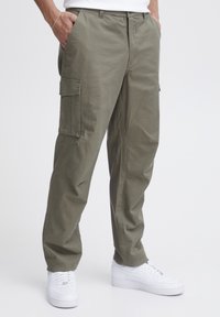 Pantalonii cargo din bumbac de culoare verde măsliniu au două buzunare laterale și picioare îngustate, asortați cu teniși albi pentru un look casual.