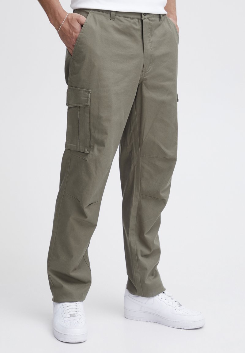 Pantalonii cargo din bumbac de culoare verde măsliniu au două buzunare laterale și picioare îngustate, asortați cu teniși albi pentru un look casual.