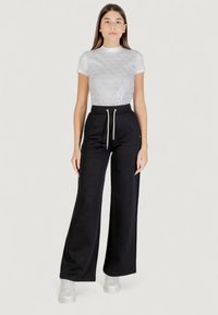 Pantalones de chándal negros de pierna ancha con cintura con cordón y acentos dorados, combinados con una blusa ajustada de textura blanca que presenta un patrón geométrico.
