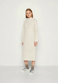 Abito a coste color crema con maniche lunghe e collo alto, abbinato a calzini grigi e sneakers bianche con strisce grigie.