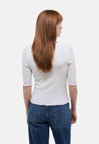 Top en tricot côtelé blanc à manches courtes et bords festonnés, associé à un jean bleu taille haute. Surface texturée visible.