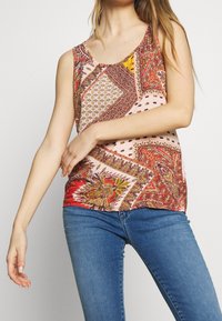 Débardeur multicolore avec un mélange de motifs paisley et géométriques, doté d'un col rond et d'un tissu léger. Associé à un jean bleu.