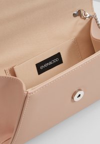 Intérieur de sac synthétique rose blush à texture lisse, avec une étiquette de marque et une fermeture à pression pour un accès sécurisé.