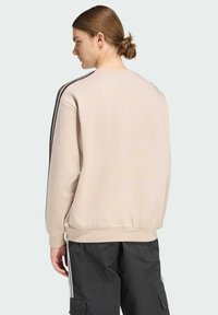 Béžová mikina s okrúhlym výstrihom, elastickými manžetami a lemom; obsahuje čierne bočné pruhy. Nosená s čiernymi cargo nohavicami.