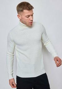Pull à col roulé en crème clair, en maille côtelée. Coupe ajustée avec des manches longues et une texture lisse, doté d'un col haut.
