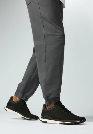 Zwarte sportieve schoenen met gaas zijkanten, een gestructureerde afwerking en witte rubberen zolen, gecombineerd met grijze tapered joggingsbroeken.