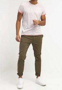 T-shirt grigio a maniche corte con bordi rosa, con testo bianco. Abbinato a pantaloni verde oliva e sneakers bianche. Look casual.