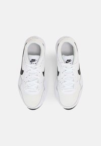 Bijele Nike Air tenisice s crnim akcentima, mrežasta gornjište, podstavljena ovratnik i vezice. Imaju okrugli vrh i teksturirani gumeni potplat.