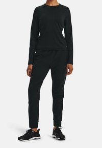 Svart långärmad topp och avsmalnande byxor i slät tyg. Outfiten kombineras med svarta sportskor med vita sulor och snören.