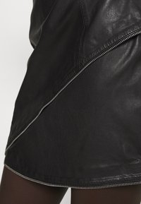 Gonna in pelle nera con dettaglio della zip diagonale, texture liscia e silhouette aderente, che enfatizza un design contemporaneo.