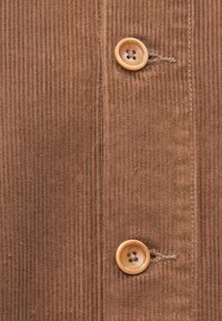 Brunt kordfløyelstoff med vertikal ribbestruktur, med to lysebrune knapper med fire hull, sydd langs midten.