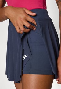 Gonna sportiva navy con design a strati, texture morbida e pantaloni aderenti sotto. Logo bianco nella parte inferiore sinistra.