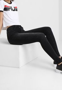 Svarta tajta jeans med hög midja, gjorda av denim, tillsammans med en vit croppad t-shirt med en djärv grafisk design och svarta sneakers.