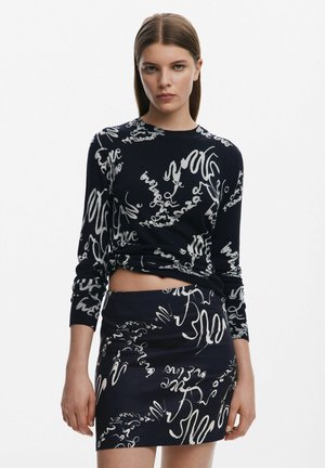 Top lungo a maniche lunghe blu navy cropped e gonna coordinata con motivi astratti bianchi. Il tessuto sembra morbido, con una texture liscia e un design aderente.