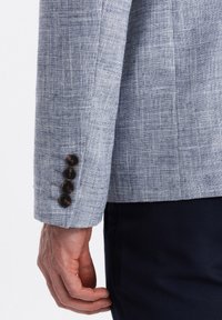 Hellblaues Leinenblazerärmel mit einer strukturierten Webart, ausgestattet mit vier dunkelbraunen Knöpfen und einem geraden Schnitt am Bündchen.