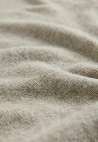 Béžová tkanina s jemným, textúrovaným povrchom, ktorý obsahuje mierne vlny a jemný tkaný vzor. Vhodná pre odevy alebo interiérové textílie.