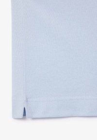 Polo bleu clair en coton texturé. Présente un ourlet fendu et des coutures discrètes le long des bords.