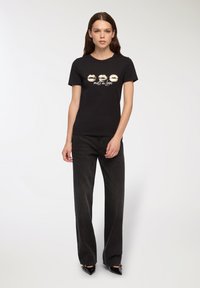 Czarny bawełniany t-shirt z nadrukiem złotych ust i napisem "melt in love". W zestawie z czarnymi, wysokim stanem spodniami w szeroką nogawkę i spiczastymi szpilkami.