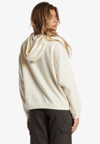 Felpa con cappuccio crema caratterizzata da una vestibilità rilassata, polsini a costine e una grande tasca posteriore. Tessuto morbido con una superficie liscia simile al cotone.