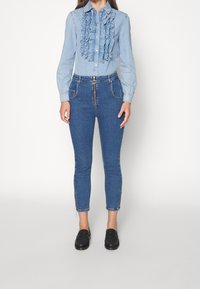 Světlemodrá denimová košile s volánkovým předním dílem, dlouhými rukávy; spárovaná s tmavomodrými slim-fit džíny, které mají boční zipy a přední zip.
