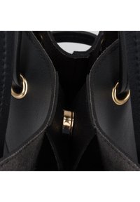 Black leather handbag interior showing smooth texture, metal hardware, and a circular gold accent with a cutout design.