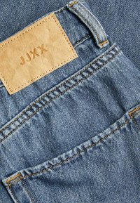 Denim jeans feature a light blue color with yellow stitching and a rectangular tan leather patch embossed with "JJXX."