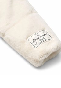 Manica in pelliccia sintetica color crema con un'etichetta rettangolare che riporta la scritta "Humankind" e testo decorativo. Texture morbida e design voluminoso.