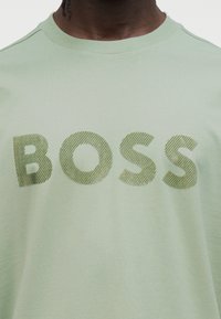 Ανοιχτό πράσινο βαμβακερό t-shirt με μεγάλο, υφασμάτινο λογότυπο «BOSS» σε πιο σκούρο πράσινο. Απλός λαιμός σε σχήμα κύκλου και απαλό, λείο ύφασμα.