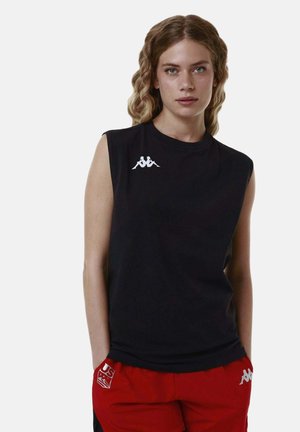 Giovane donna con capelli mossi che indossa un top nero senza maniche e pantaloncini rossi con loghi bianchi del marchio su sfondo semplice.